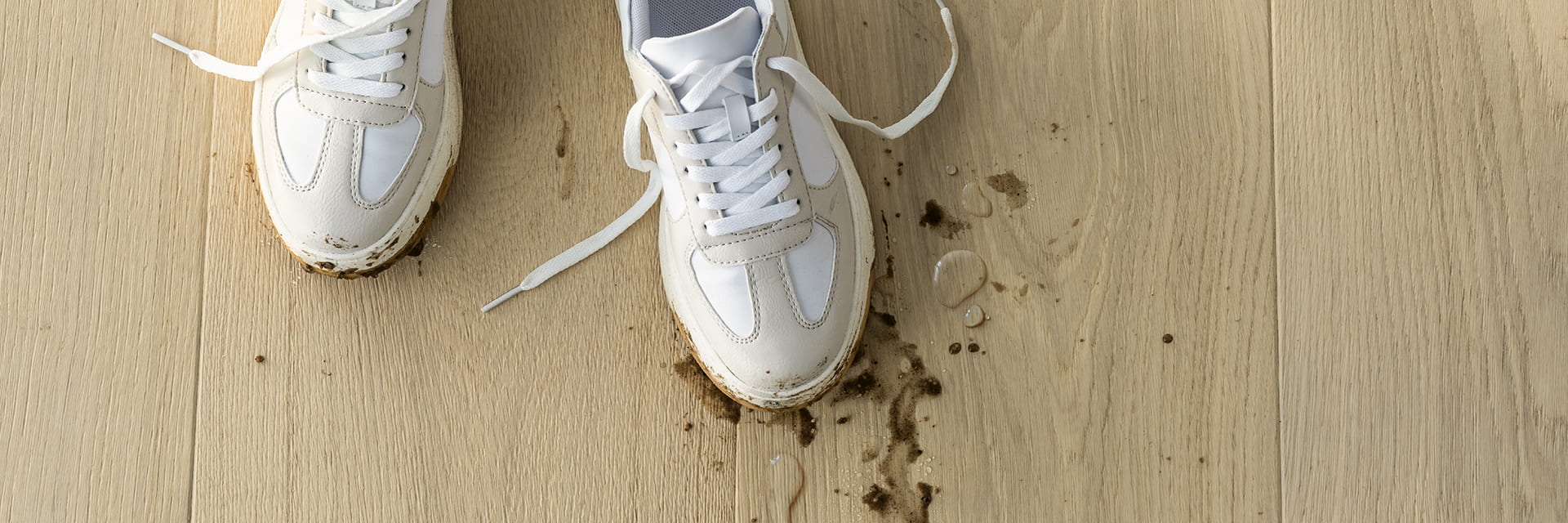nærbilde av møkkete sko med sølt gjørme og vann på et beige parkettgulv